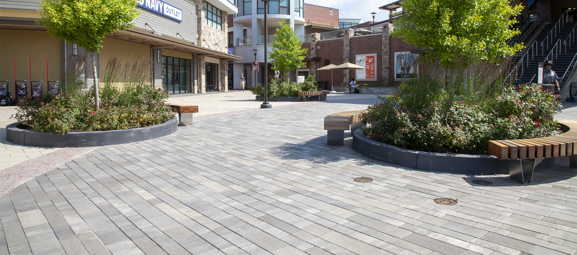 Artline in a grey hue helps delineate resting areas in a busy shopping plaza, with garden islands and park benches scattered throughout.