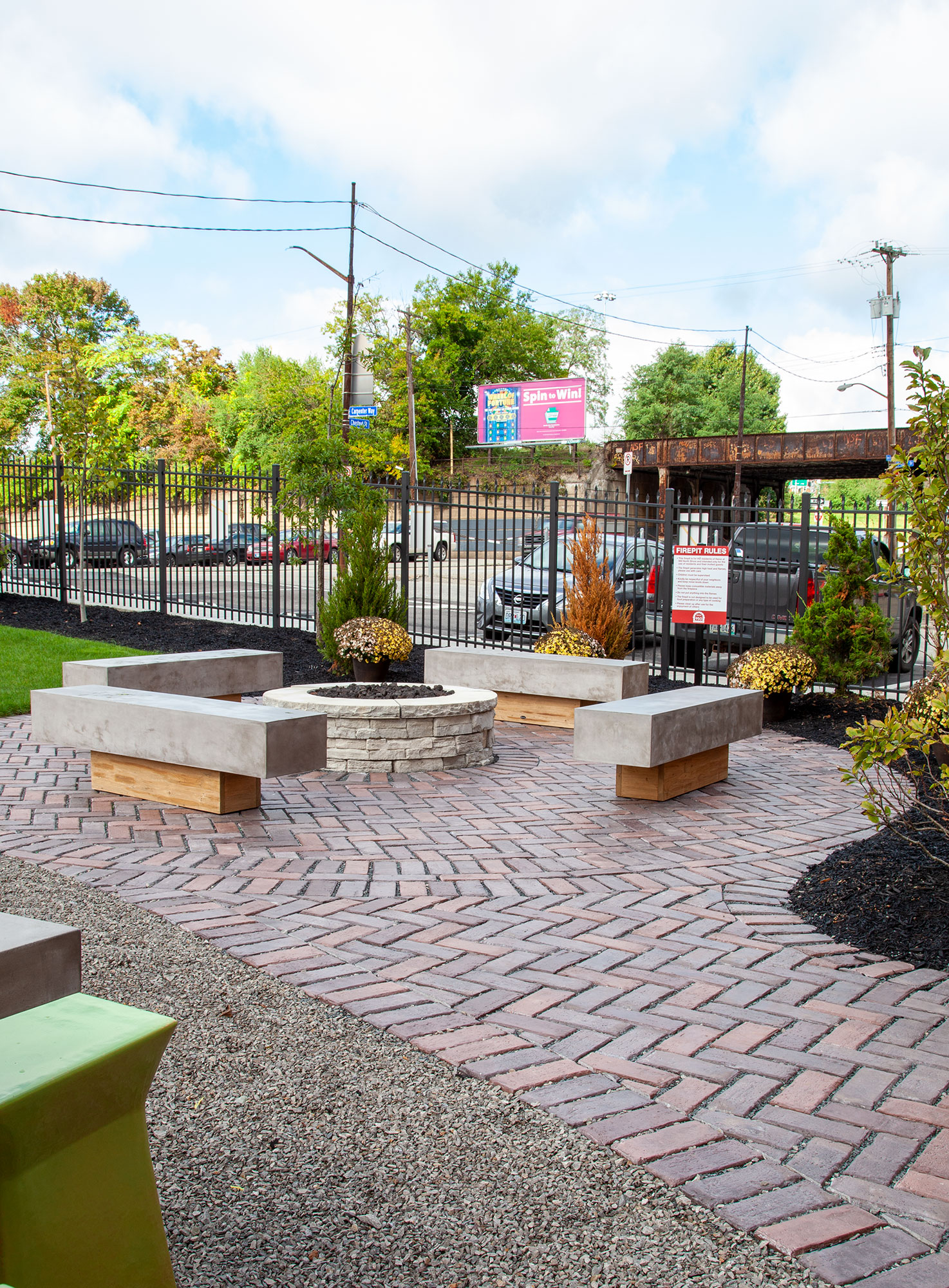 A circular fire pit and stone benches are surrounded by tri-colored Town Hall pavers, with nearby bushes adding subtle flecks of color.