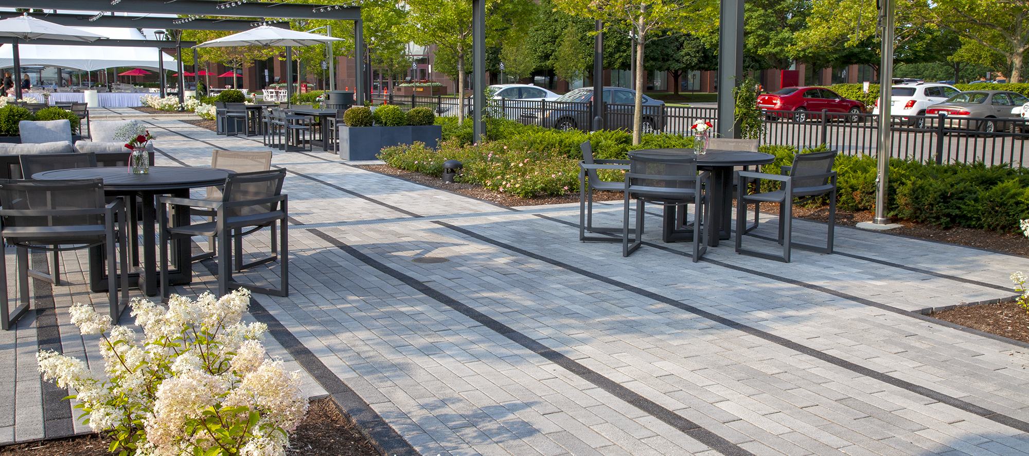 Two-toned Promenade Plank pavers delineate rows of walking spaces, with outdoor tables, chairs and umbrellas .