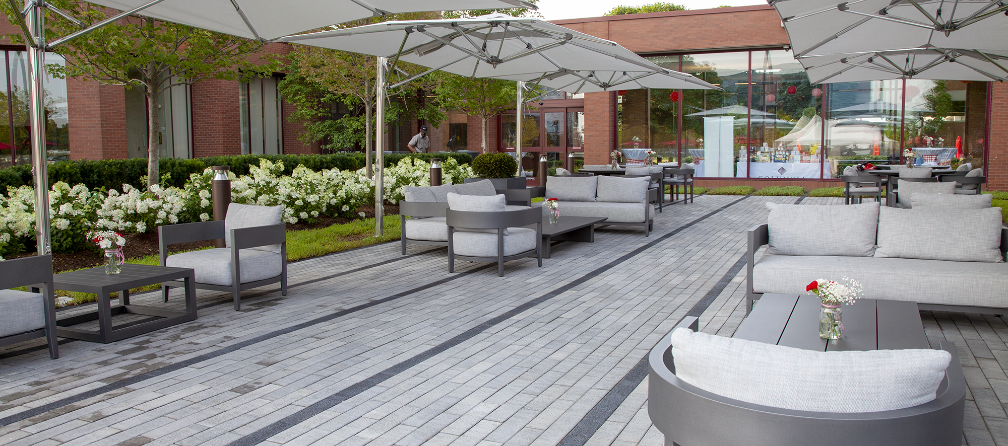 Two-toned Promenade Plank pavers delineate rows of walking spaces, with outdoor tables, chairs and umbrellas .