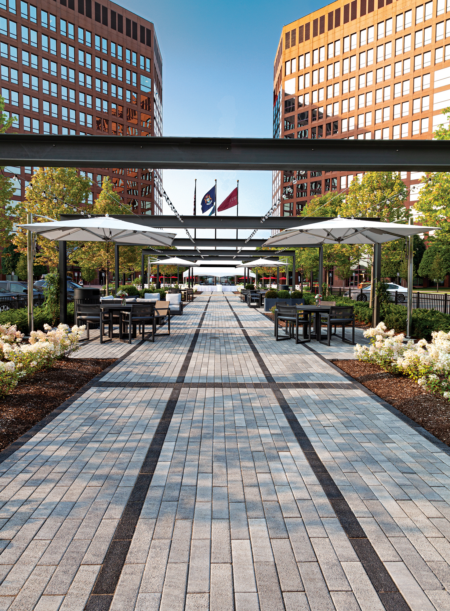 Two-toned Promenade Plank pavers create a walkway leading toward the building, with outdoor couches, tables and chairs for lounging.