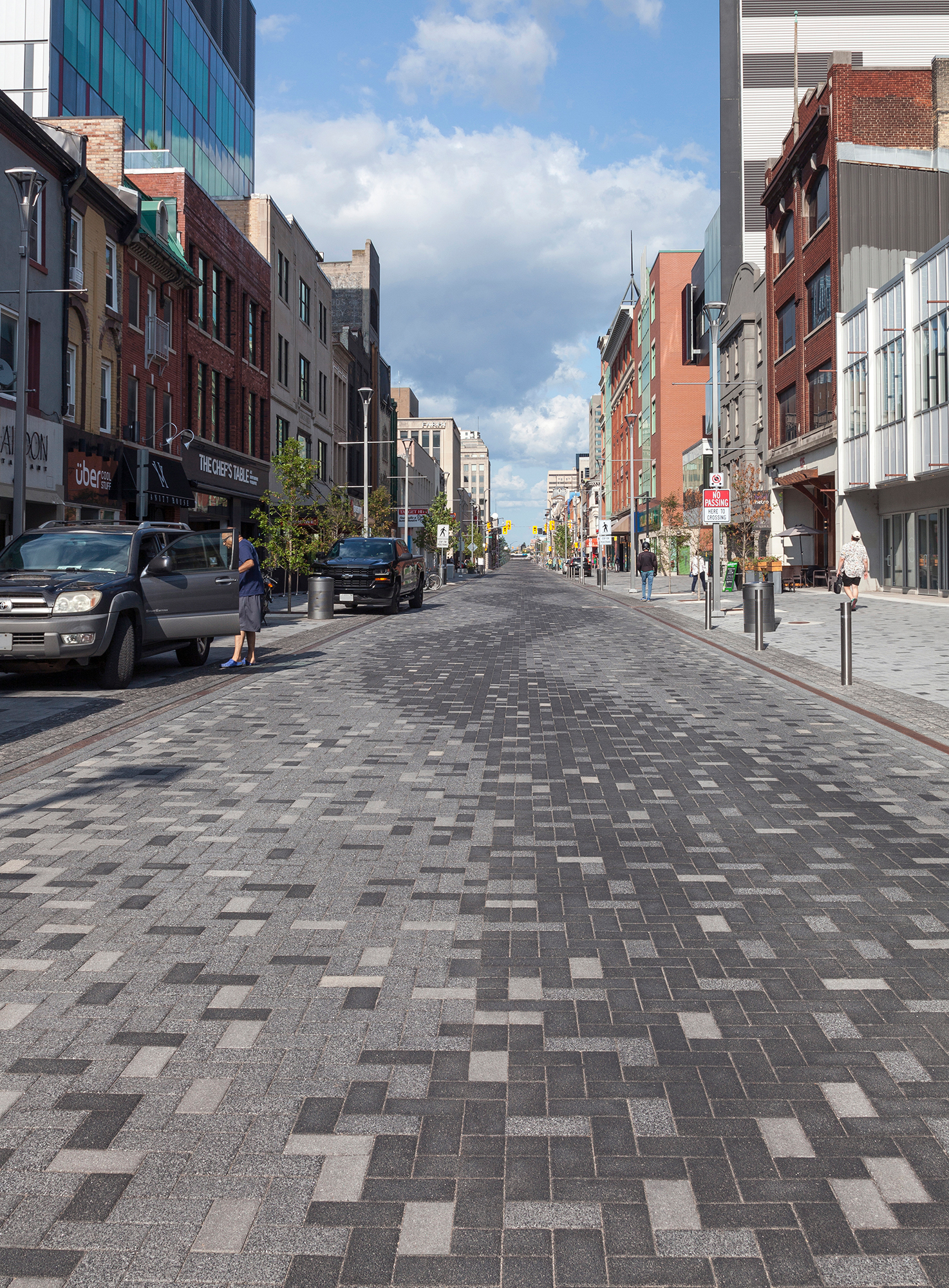 People park and walk along Dundas Place streetscape, paved with Series in pixelated patterns with a curvy zig-zag in the center.