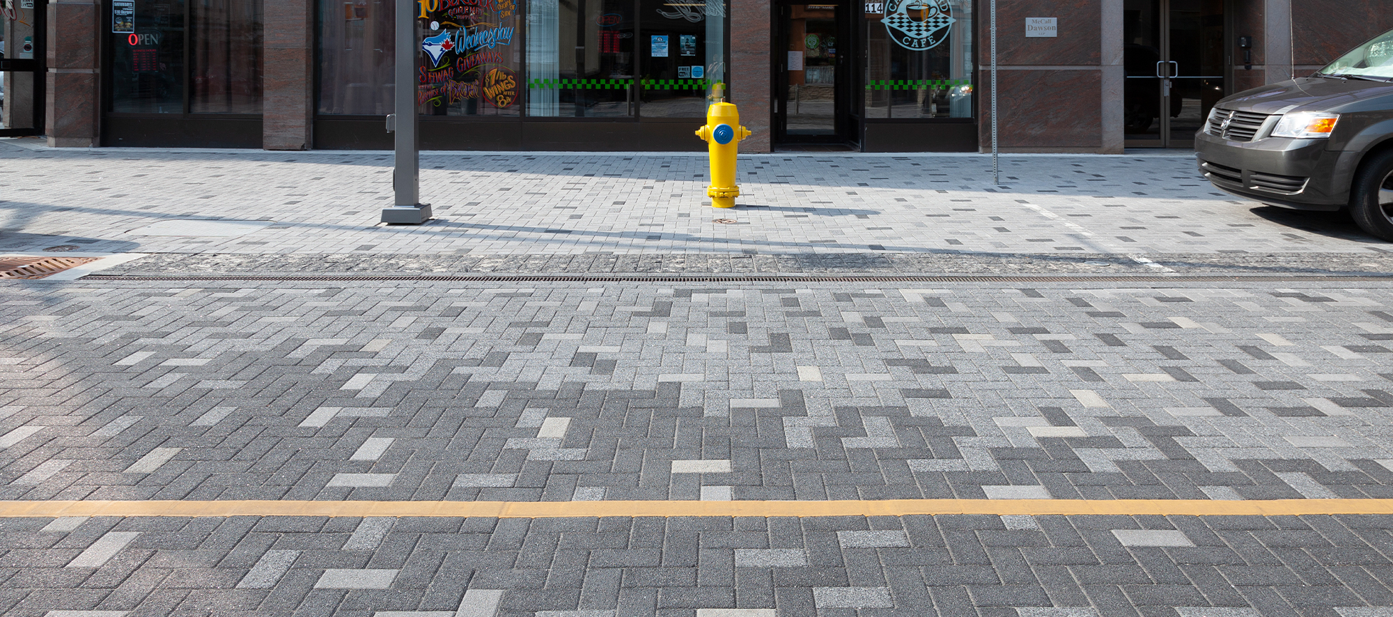 A car is parked near a hydrant at Dundas Place streetscape on Series pavers with alternating tones creating patterns and delineation.