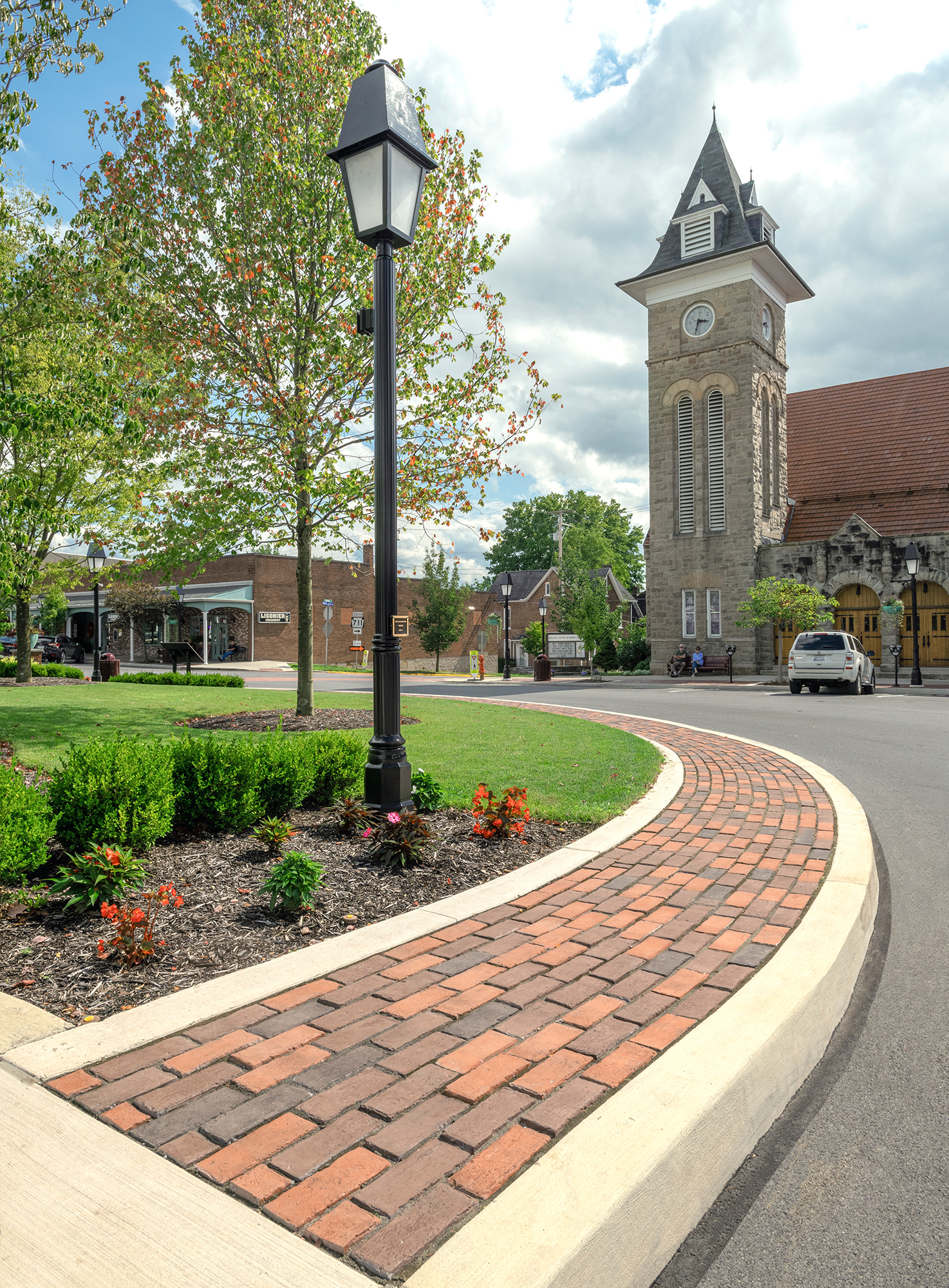 Town Hall pavers in red tones created a rounded sidewalk on the outskirts of a park across from a historic building with a clock tower.
