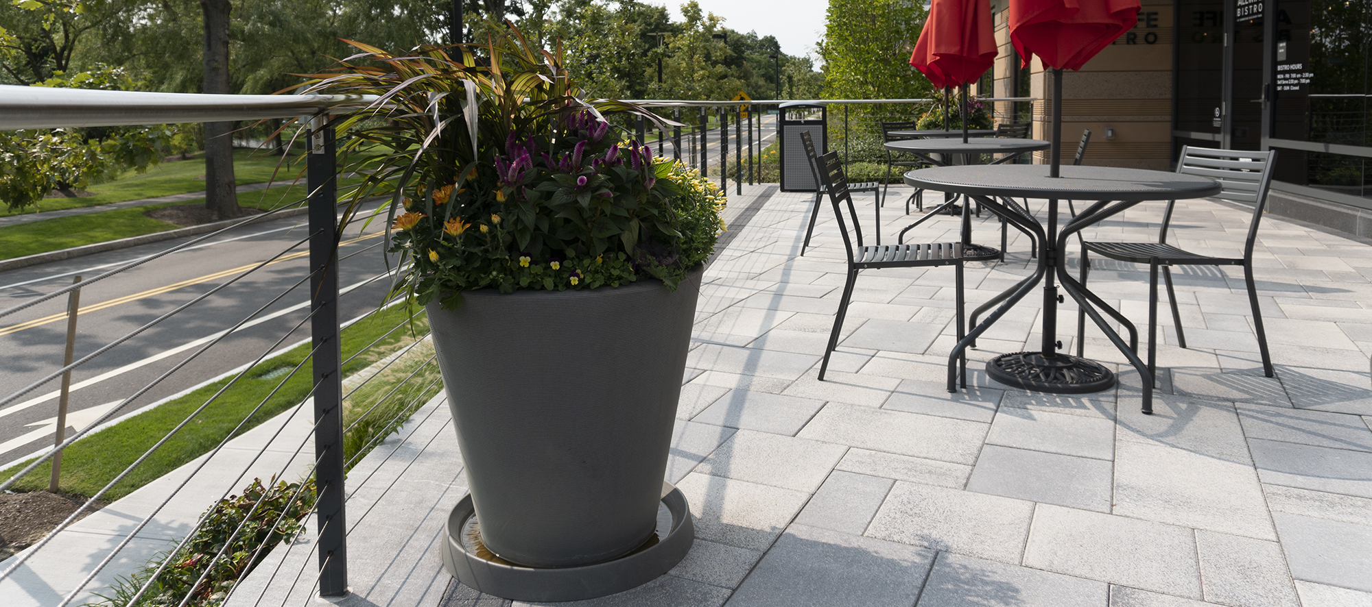 White Umbriano paver patio is enclosed by a wire railing, with a decorative seasonal plant, an outdoor table and chairs adorning the space.