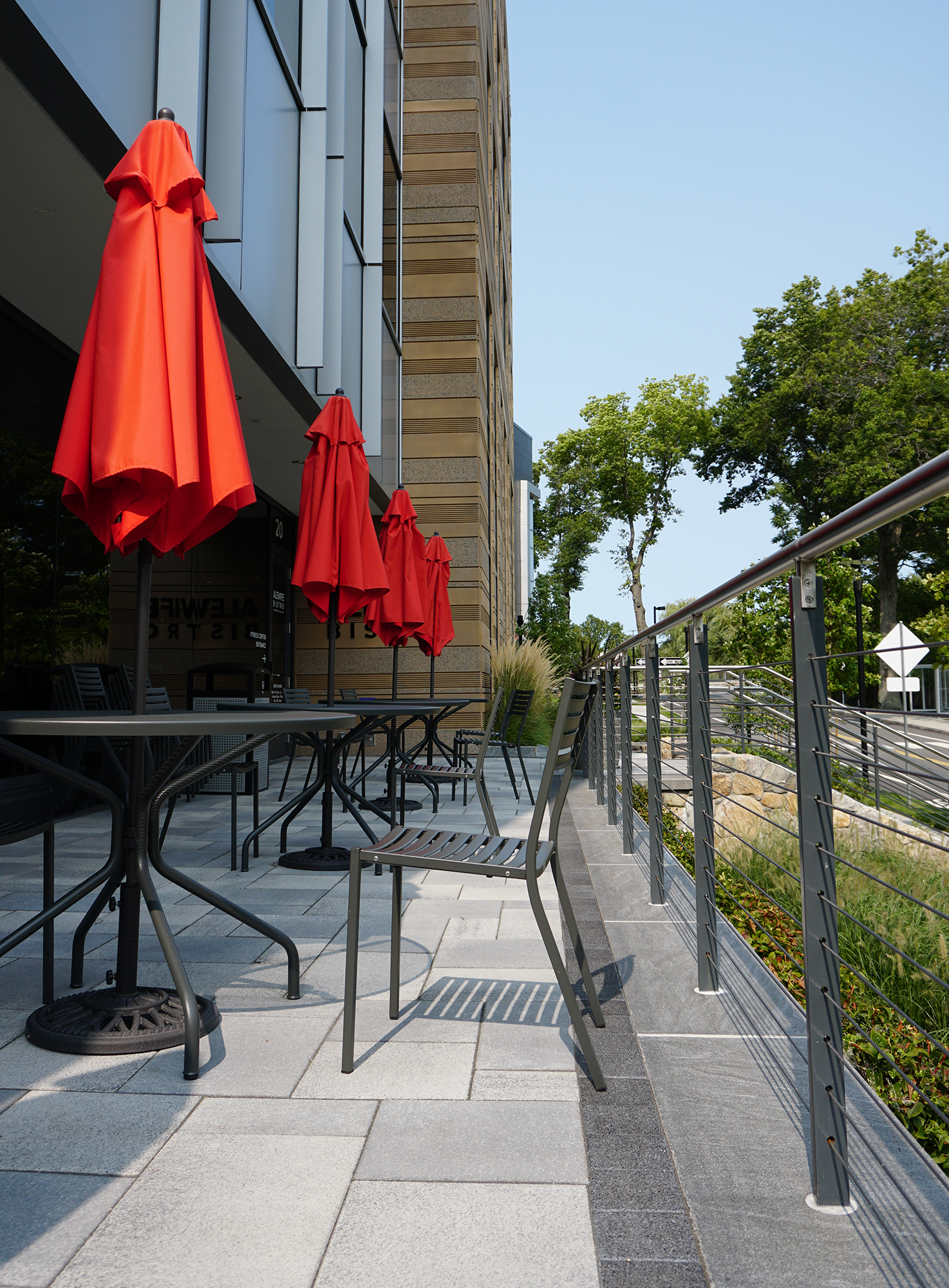 White Umbriano paver patio is enclosed by a wire railing, with an outdoor table and chairs and red umbrellas adorning the space.