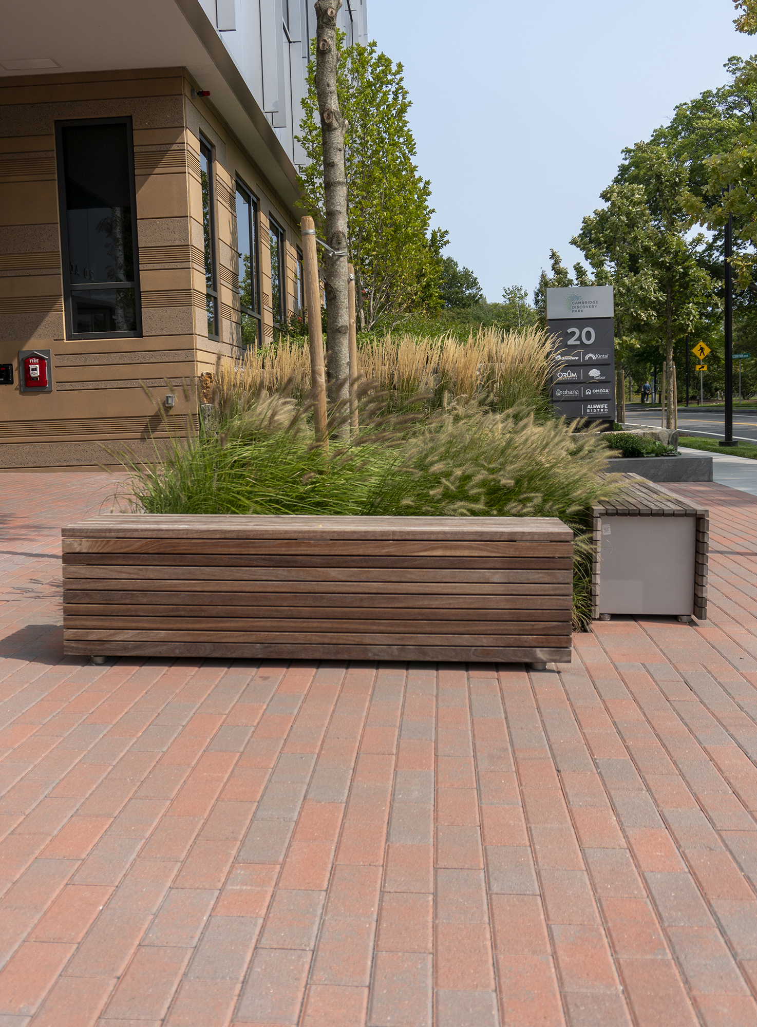 A large outdoor seated area with planted trees and a sidewalk features red Hollandstone brick pavers along the square.