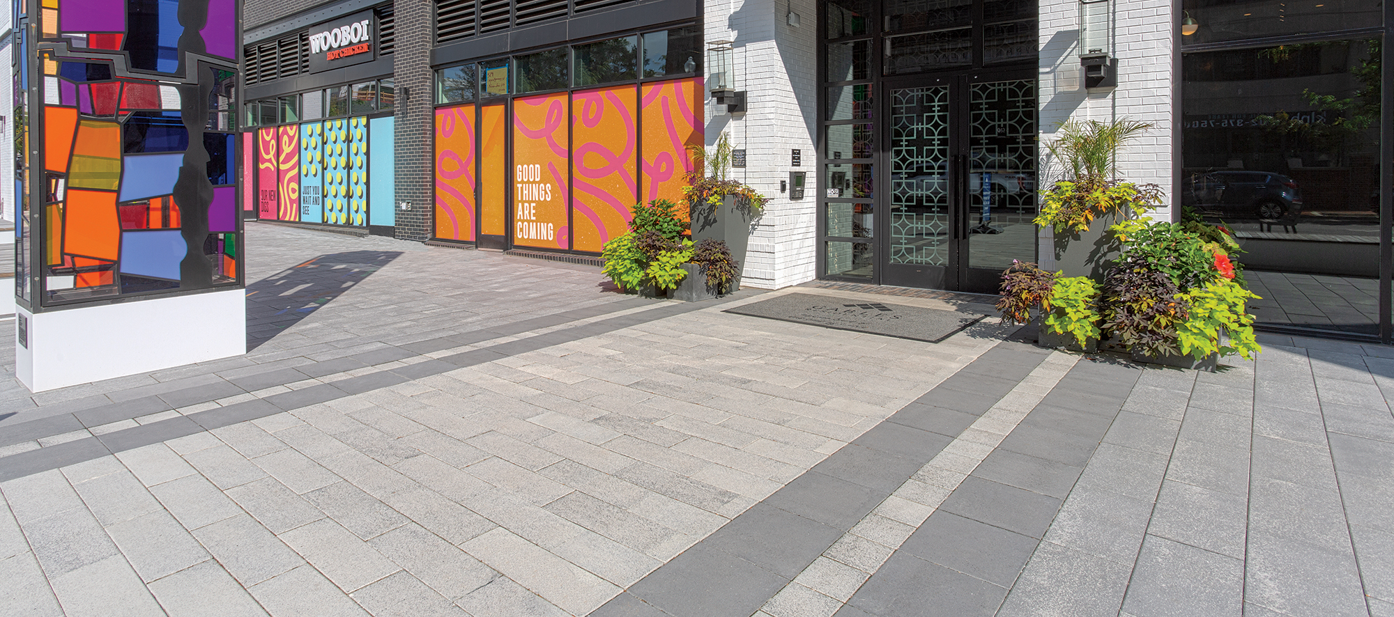 Bright colors and organic shapes of a stained glass pillar, posters, and planters contrast with muted tones and stripes of Umbriano pavers.
