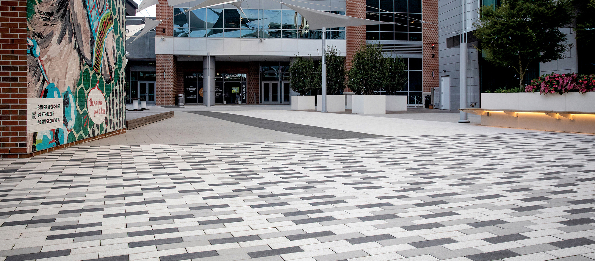 Promenade Plank pavers in a checkboard pattern transition to parallel white and black planks, guiding visitors to the building's entrance.