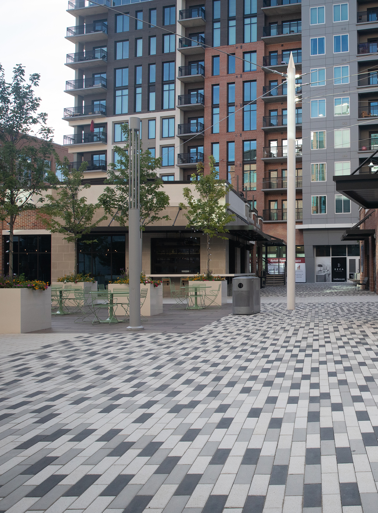 Promenade Plank pavers in a checkboard pattern guide visitors to the front entrance, as well as an outdoor eating space with large planters.