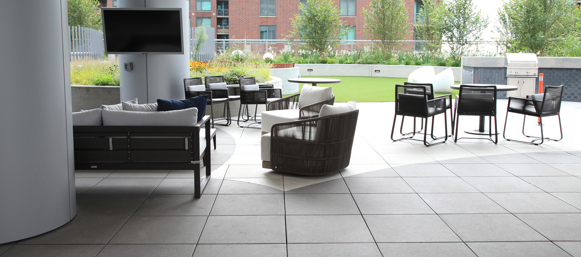 An outdoor living room with a TV and BBQ area on a circular themed roof deck created with Unilock Arcana slabs in white and grey.