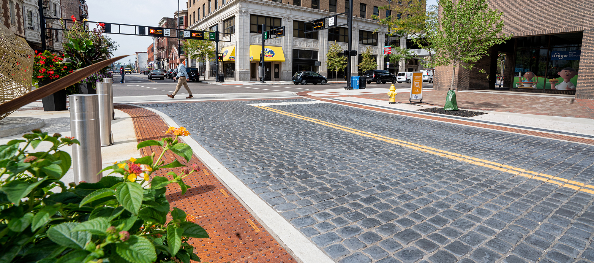 Blue Courtstone pavers occupy the roadway, with painted yellow lines dividing the lanes, and gentle soft scaping decorating street corners.
