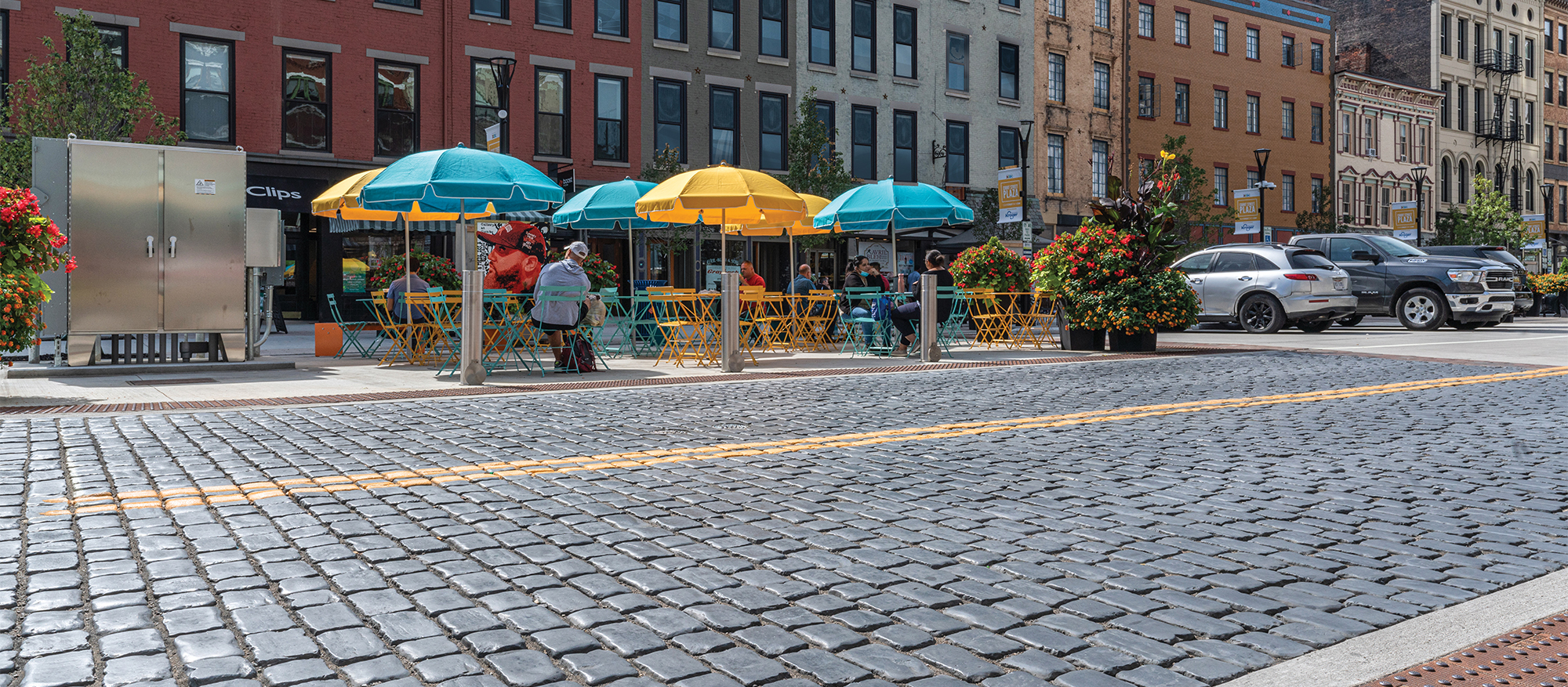 Visitors lounge street side in colorful tables and chairs, next to the main roadway that features Courtstone pavers in a deep blue hue.