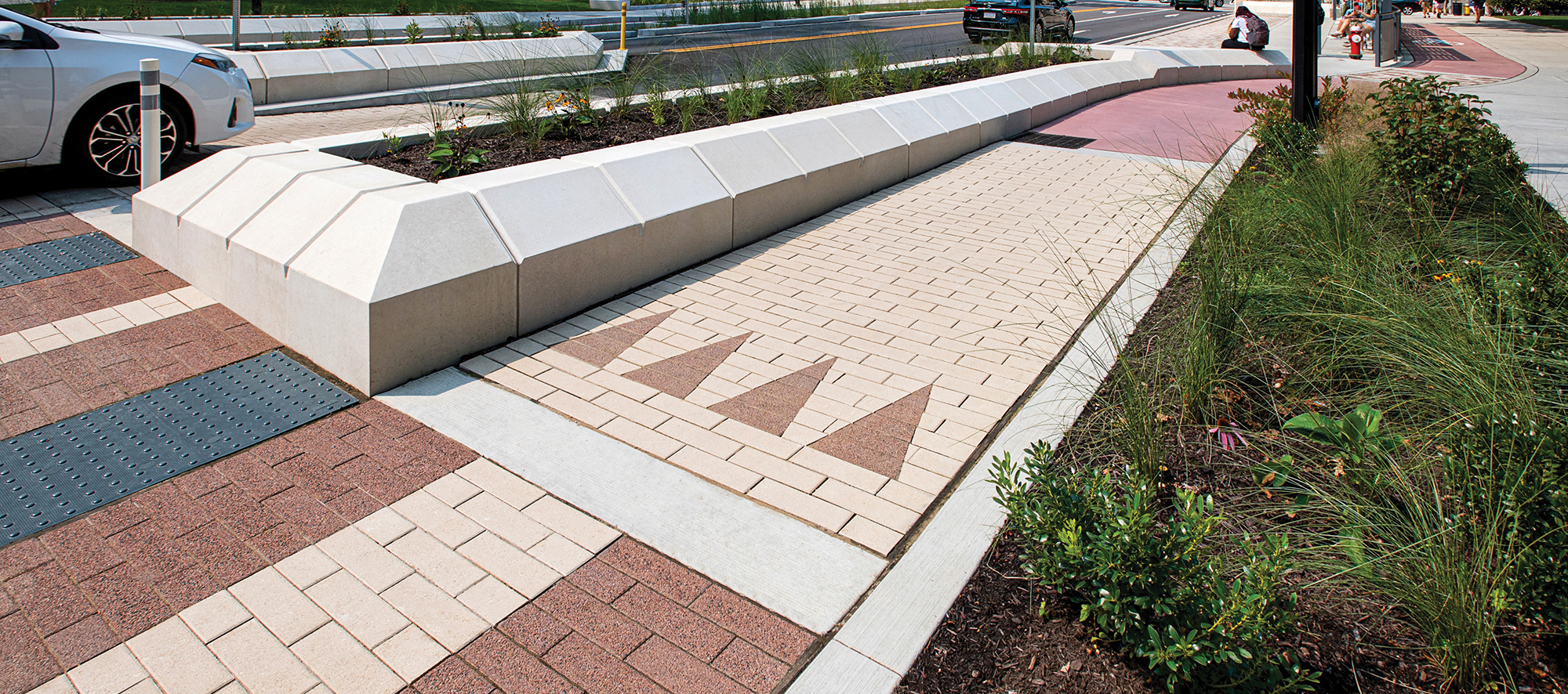 Cars drive on a streetscape with curb gardens, landscaping and Promenade pavers in contrasting colors creating stripes and arrows.
