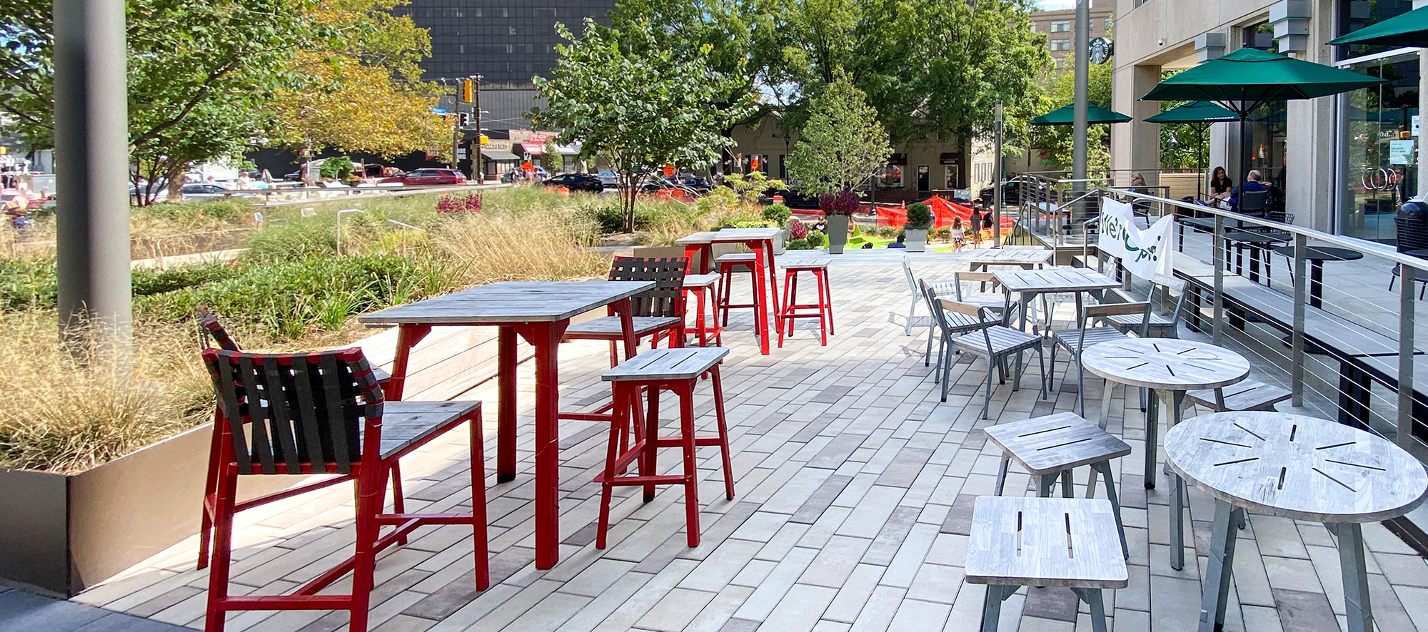 A public dining area made with Unilock Artline rectangular pavers in a mix of warm colors sits between a café's outdoor seating and gardens.