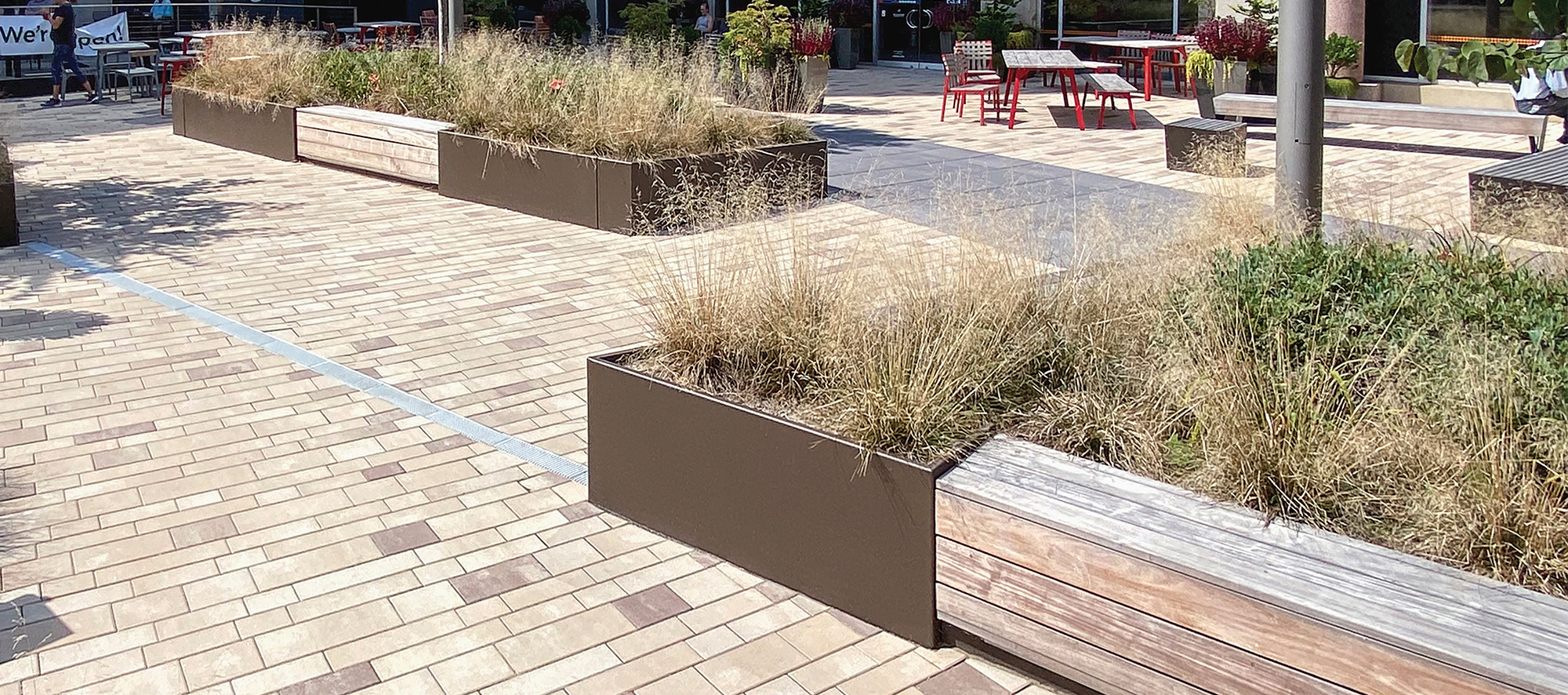 A pedestrian plaza made with Artline rectangular pavers in a mix of warm colors and a stripe of dark colors includes seating and plants.