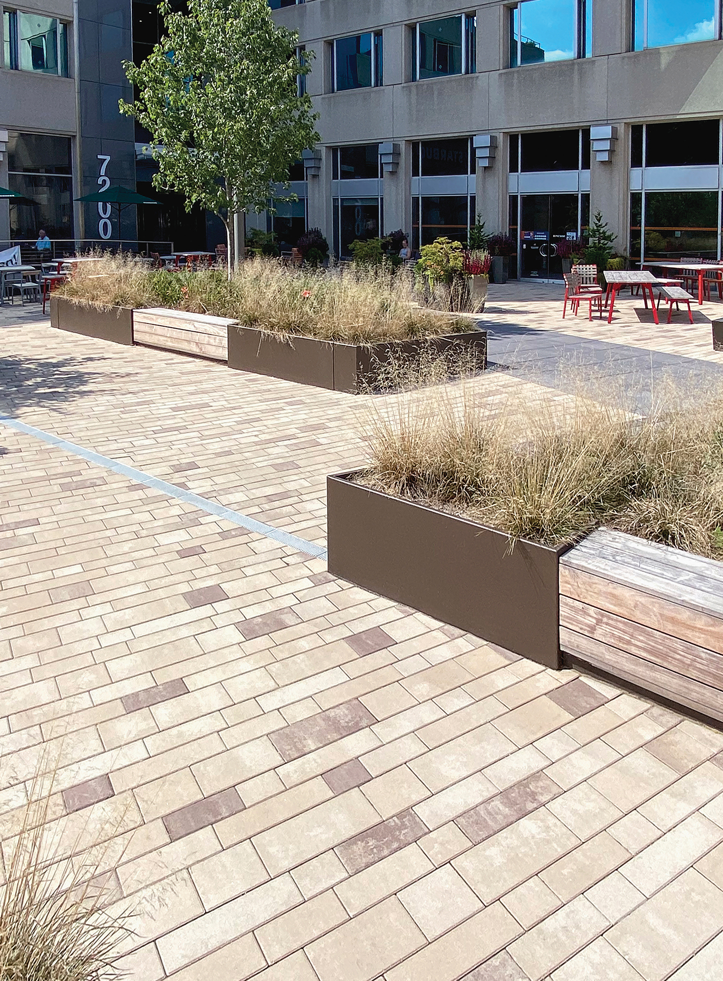 In front of a commercial building, Unilock Artline rectangular pavers in contrasting colors create a plaza with gardens and dining areas.