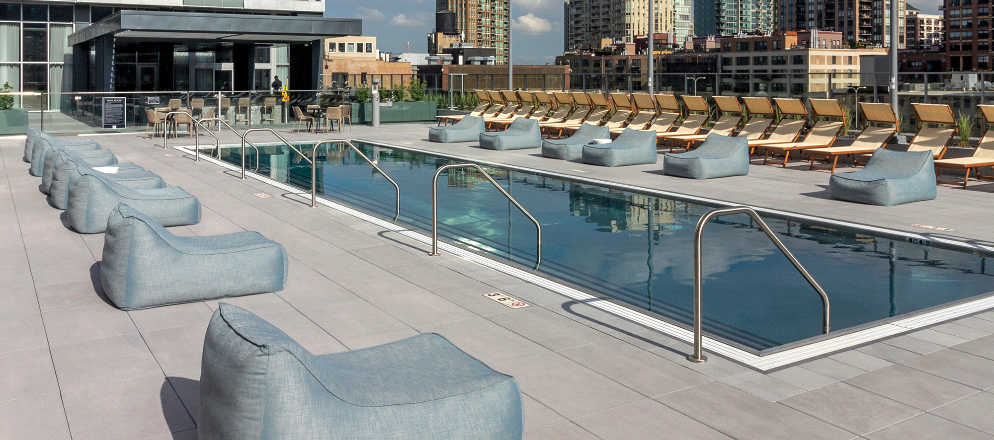 Parallel to the Chicago skyline, this roof deck features a pool, lounge chairs, and large square Unilock slabs in the color opal.