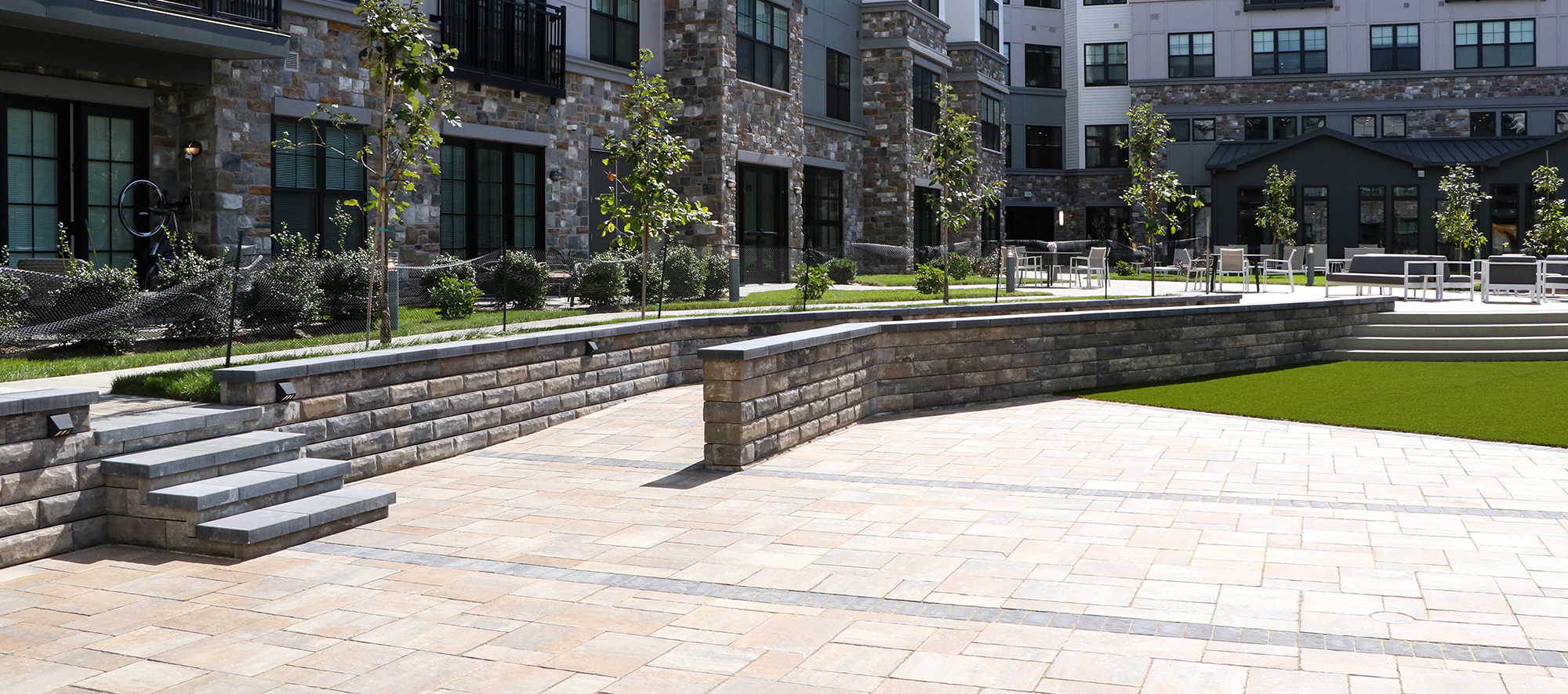 Brown Bristol Valley paver floor, with a U-Cara retaining wall and grey steps leading to an upper walkway with outdoor chairs.
