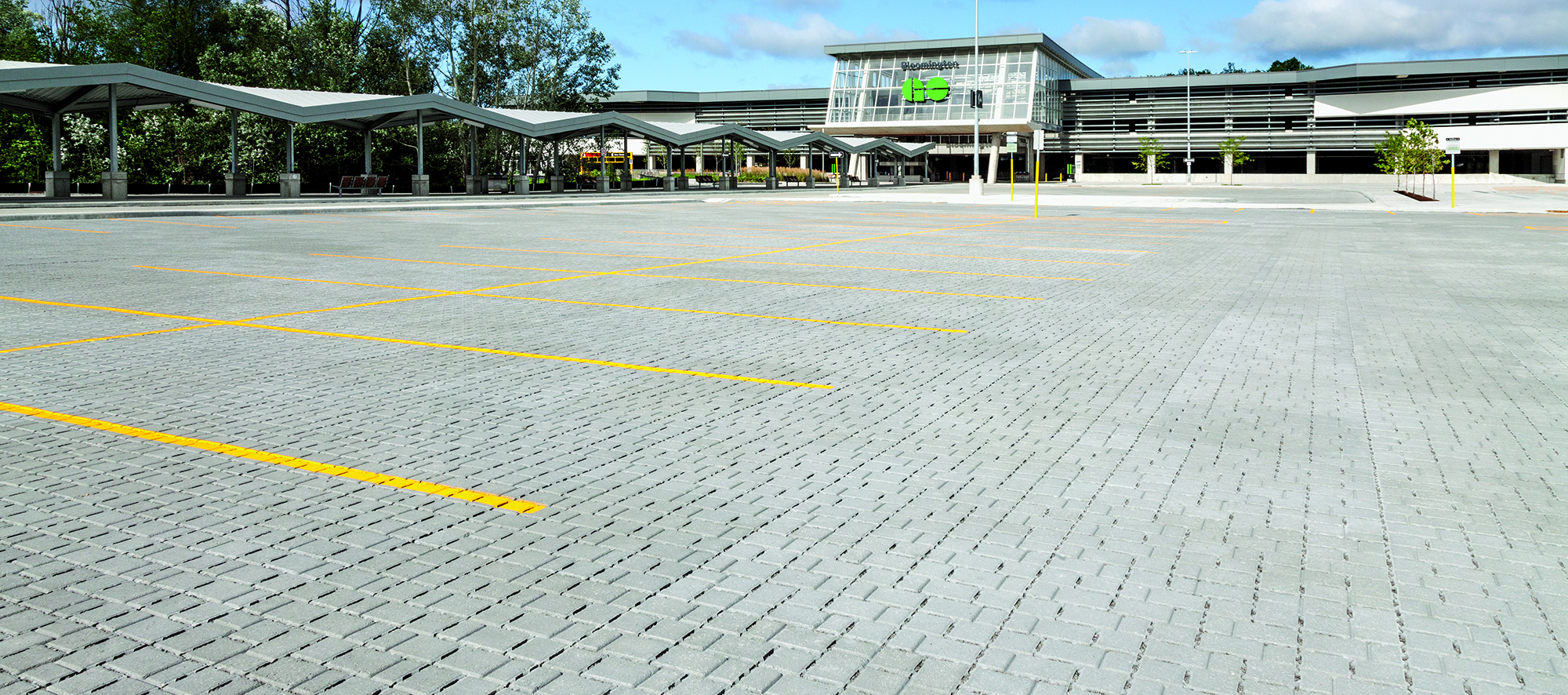 A parking lot paved in grey Eco-Optiloc permeable pavers precedes a glass and cement building with bus bays that says Bloomington GO.